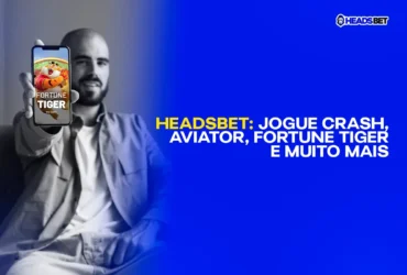 imagem em preto e branco com homem sentado e sorrindo apontando o celular em direção da tela com uma imagem colorida do jogo de cassino fortune tiger. Crash games na Headsbet: aviator, fortune tiger.